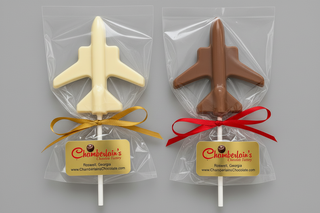 Two airplane-shaped chocolate lollipops in clear gift bags. One lollipop is white chocolate and the other is milk chocolate. 