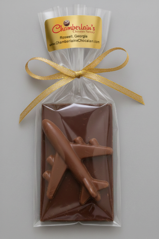 A packaged chocolate airplane featuring a dark chocolate base with a milk chocolate airplane sealed in a clear bag with a gold ribbon and a branded Chamberlain's label 