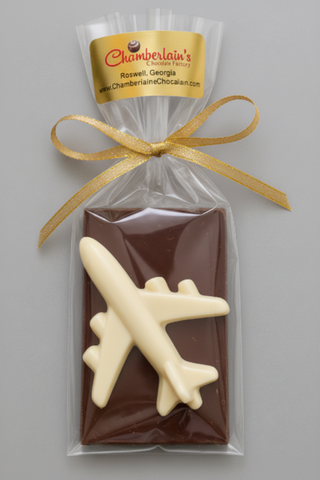 A packaged chocolate bar featuring a dark chocolate base with a white chocolate airplane sealed in a clear bag with a gold ribbon and a branded Chamberlain's label 