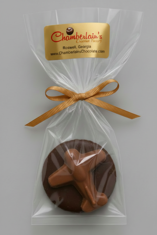 A round chocolate covered Oreo with a white chocolate airplane, individually wrapped in a clear cellophane bag with a silver ribbon and a white label from Chamberlain's Chocolate