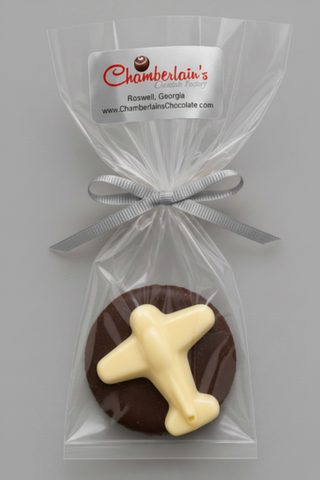 A round chocolate Oreo with a white chocolate airplane, individually wrapped in a clear cellophane bag with a silver ribbon and a white label from Chamberlain's Chocolate