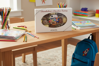 Chamberlain's Chocolate Factory Back to School chocolate gift box displayed on a classroom desk surrounded by colored pencils, notebooks, and a blue backpack, Atlanta Georgia