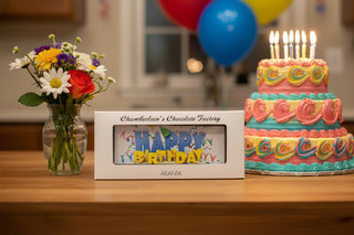 Happy Birthday Large Chocolate Bar With Edible Image next to colorful birthday cake and flowers on a festive table.