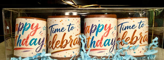 Close-up of 4 artisan chocolate shot glasses with vibrant rainbow-colored edible birthday prints and blue crinkle paper, gift boxed with gold bow, made at Chamberlain's Chocolate in Atlanta, GA
