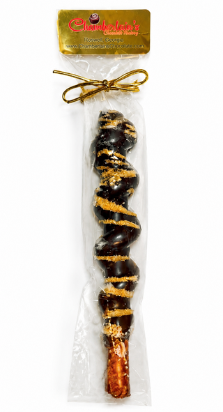 A packaged dark chocolate-covered pretzel rod with gold drizzle and sugar crystals, sealed in a clear plastic bag with a gold bow from Chamberlains Chocolate Factory

