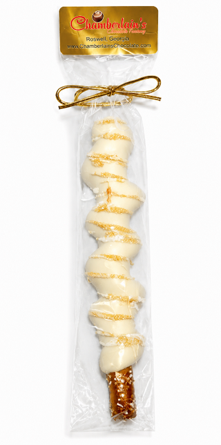 A packaged white chocolate-covered pretzel rod with gold drizzle and sugar crystals, sealed in a clear plastic bag with a gold bow from Chamberlains Chocolate Factory