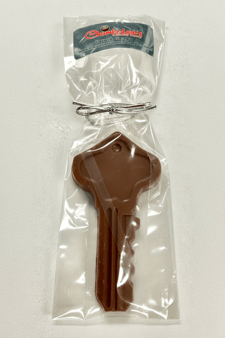 Chocolate key shaped like a house key in clear packaging with a brand label on a white background