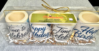 Top view of 4 artisan white chocolate shot glasses with blue edible birthday prints in a clear gift box with Chamberlain's Chocolate label, Roswell Georgia