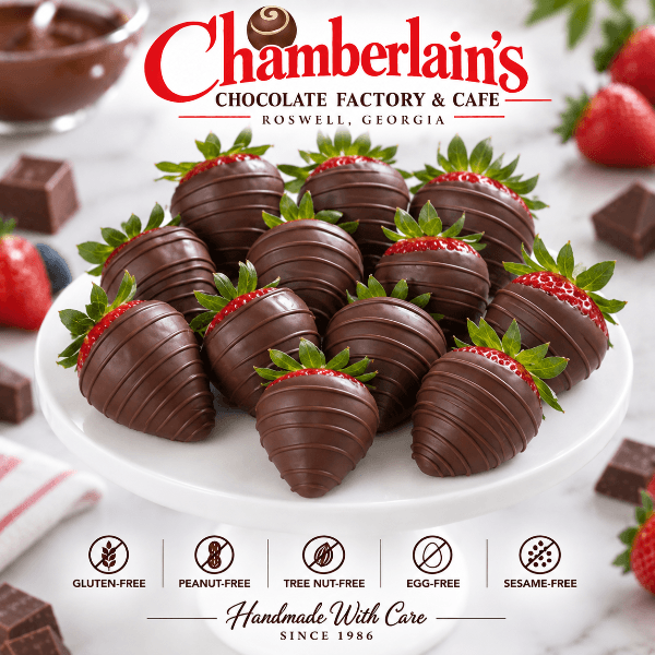 One dozen semi-sweet dark chocolate covered strawberries piled on a white cake stand, surrounded by fresh strawberries and blueberries — gourmet chocolate gift from Chamberlain's in Roswell, Georgia"