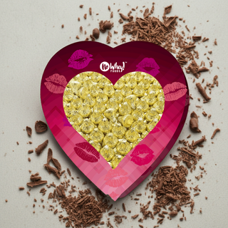 Heart-shaped box of allergen friendly vegan chocolates filled with shiny wrapped kisses on a bed of chocolate shavings.