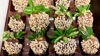 Chocolate Dipped Strawberries with Almonds arranged in a box, topped with chopped almonds and fresh green leaves.