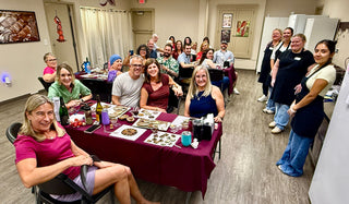 Adults smiling and enjoying a BYOB chocolate making class at Chamberlain's Chocolate Factory in Roswell, GA, with chocolate creations and drinks on burgundy-draped tables