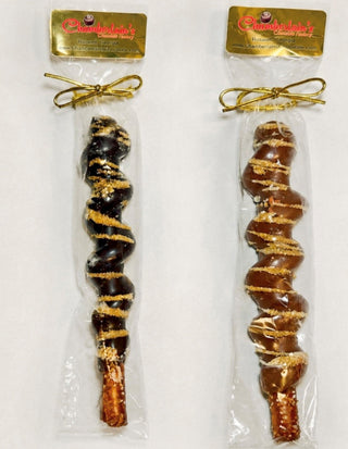 Two packaged chocolate-covered pretzel rod with gold drizzle and sugar crystals, sealed in a clear plastic bag with a gold bow from Chamberlains Chocolate Factory