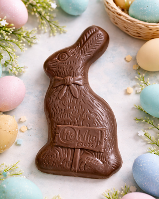 Allergy Friendly Milkless Vegan Easter Rabbit made of chocolate, surrounded by pastel colored eggs and greenery.