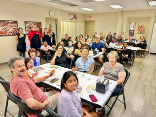 Packed room of families and adults enjoying a giant chocolate bar making class at Chamberlain's Chocolate Factory in Roswell, GA, with completed chocolate bars and toppings on the tables and staff in aprons