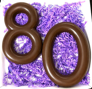 Open gift box with molded milk chocolate number 80 nestled in purple paper shred, custom chocolate milestone birthday gift from Chamberlain's Chocolate Factory