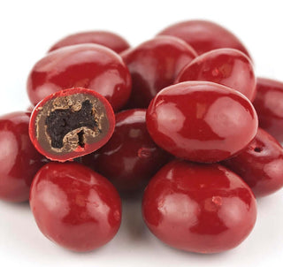 Pile of glossy red candy-coated chocolate cherries, one cut open to show the chewy dried cherry center inside milk chocolate