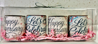 Set of 4 solid chocolate shot glasses with elegant silver script edible 'Happy Anniversary' and 'Let's Celebrate' prints, nestled in pink crinkle paper in a clear gift box with silver bow, artisan-made at Chamberlain's Chocolate, Roswell GA