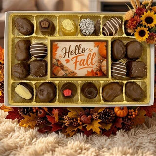 An autumn-themed chocolate gift box filled with assorted chocolates, decorated with fall leaves, pumpkins, and a sunflower bouquet, set on a shag rug in a cozy living room.