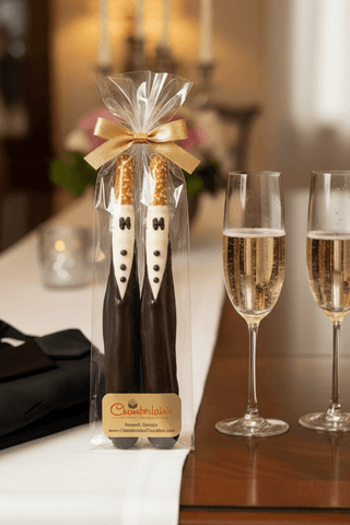 Tuxedo chocolate-dipped pretzel rod groom wedding favors in clear bag with gold bow on elegant reception table with champagne flutes candles and white floral decor