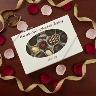 Chamberlains Chocolate Factory white gift box with oval window showing assorted dark chocolate truffles and caramels on dark wood surface with rose petals and gold ribbon, premium half pound chocolate gift