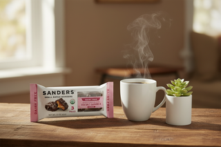 Sanders dairy-free dark chocolate sea salt caramels bag on wooden surface next to coffee cup and small plant, vegan allergen-friendly snack lifestyle photography