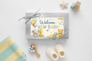 Welcome New Baby silver chocolate gift box with silver bow displayed as flat lay surrounded by soft pastel baby items including knit blanket booties and rattle, new baby shower gift