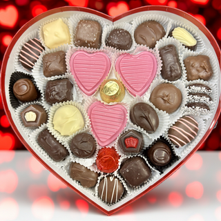 Two Pound Heart-shaped box of chocolates with a red ribbon next to red roses on a wooden surface
