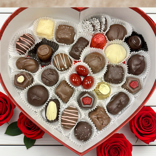 Two Pound Heart-shaped box of chocolates with a red ribbon next to red roses on a wooden surface
